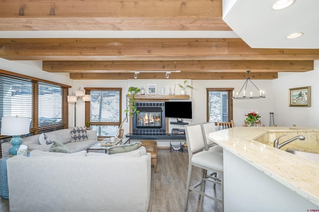 living room featuring recessed lighting, an inviting chandelier, a glass covered fireplace, wood finished floors, and beamed ceiling