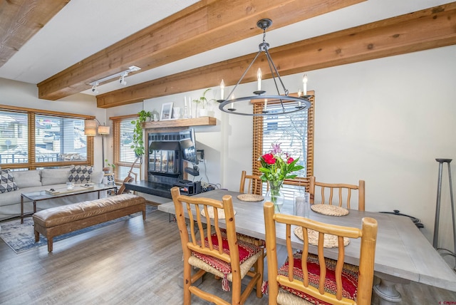 dining space featuring a tiled fireplace, beam ceiling, and wood finished floors