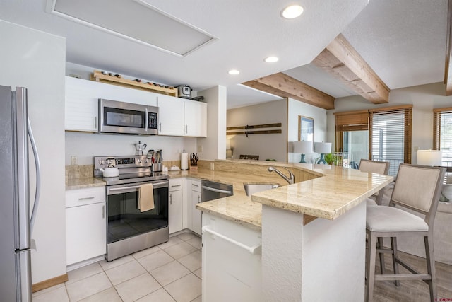 kitchen featuring a peninsula, a sink, white cabinets, appliances with stainless steel finishes, and a kitchen bar