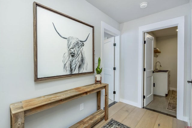 hallway featuring light wood finished floors, a sink, and baseboards