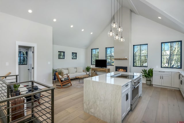 kitchen featuring light stone counters, a center island, stainless steel range, light wood-style flooring, and high vaulted ceiling