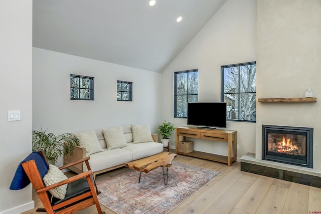 living room featuring high vaulted ceiling, hardwood / wood-style floors, a glass covered fireplace, and recessed lighting