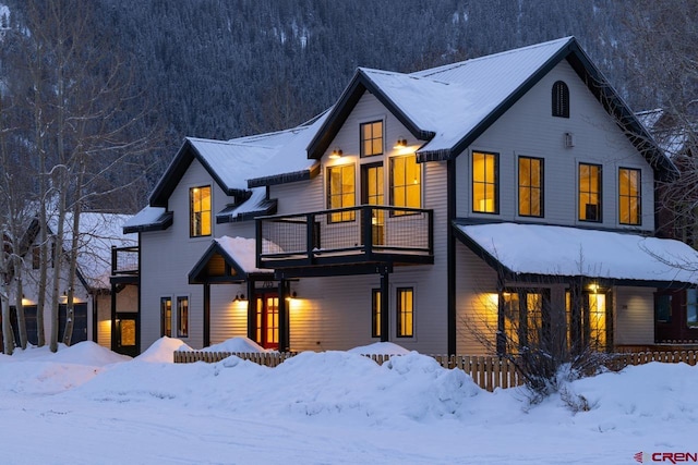 snow covered back of property with a balcony and a view of trees