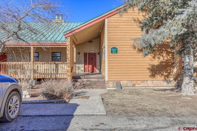 doorway to property with a porch, metal roof, and a chimney