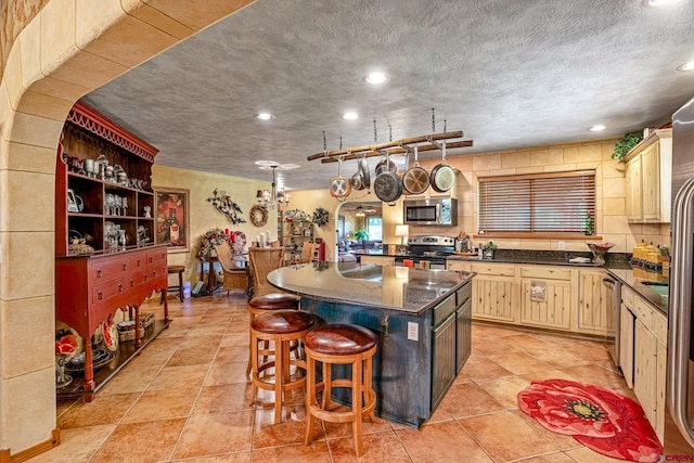 kitchen featuring dark countertops, a kitchen island, appliances with stainless steel finishes, a breakfast bar, and a textured ceiling