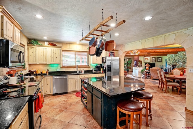 kitchen with arched walkways, stainless steel appliances, a kitchen bar, and a sink