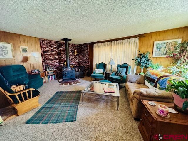 living area with a wood stove, wooden walls, carpet floors, and a textured ceiling