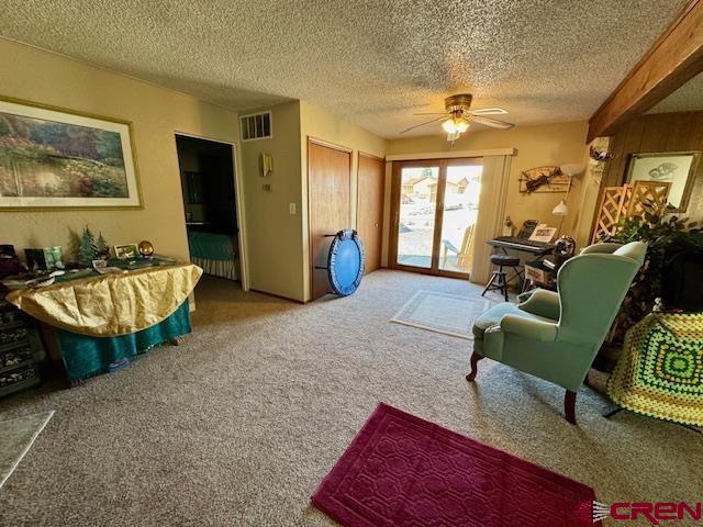 sitting room with carpet, visible vents, ceiling fan, and a textured ceiling