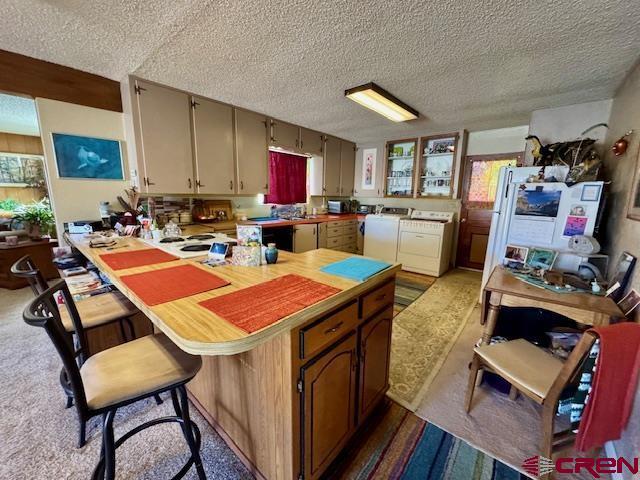 kitchen featuring a textured ceiling, a peninsula, a breakfast bar, white fridge, and washer and clothes dryer