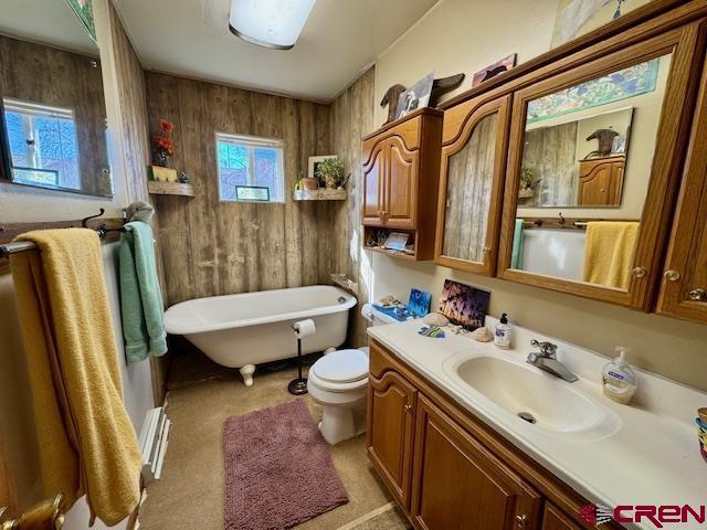 full bath with toilet, a freestanding tub, vanity, and wooden walls