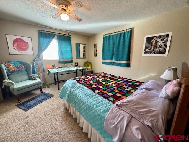 bedroom with a textured ceiling, a ceiling fan, carpet flooring, and a textured wall