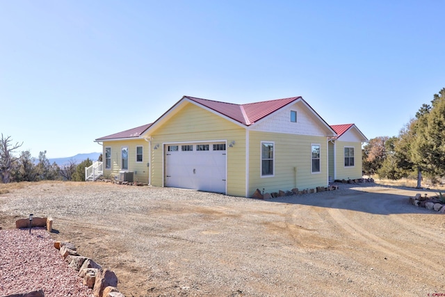 view of front of house with driveway, an attached garage, central AC unit, and metal roof