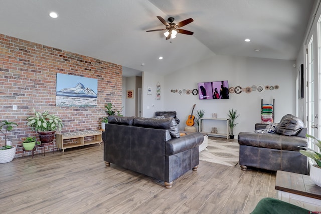 living area with a ceiling fan, vaulted ceiling, brick wall, and wood finished floors