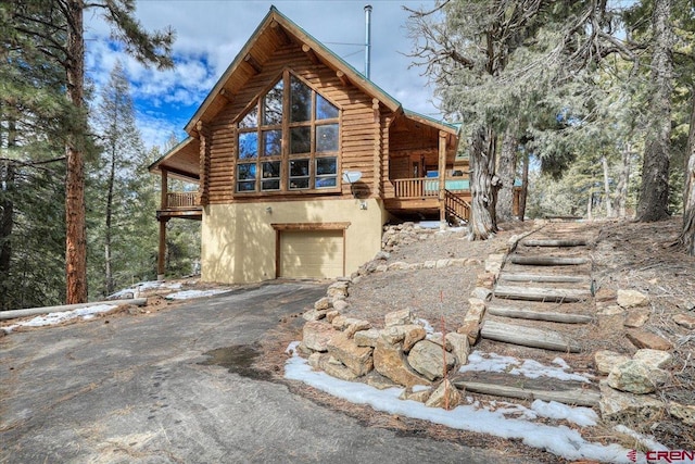 exterior space with driveway, an attached garage, log siding, and stucco siding