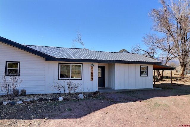 view of front facade with board and batten siding, metal roof, driveway, and a carport