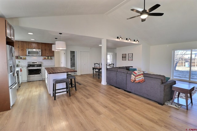 kitchen featuring butcher block counters, light wood-style flooring, decorative backsplash, appliances with stainless steel finishes, and open floor plan