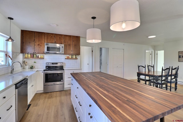 kitchen with light wood-style flooring, butcher block countertops, appliances with stainless steel finishes, a sink, and backsplash