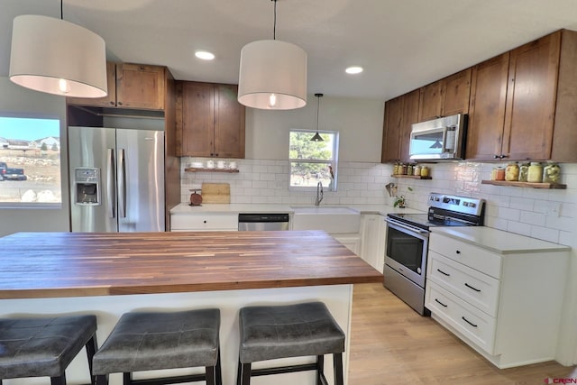 kitchen featuring light wood-style flooring, butcher block countertops, a sink, appliances with stainless steel finishes, and decorative backsplash