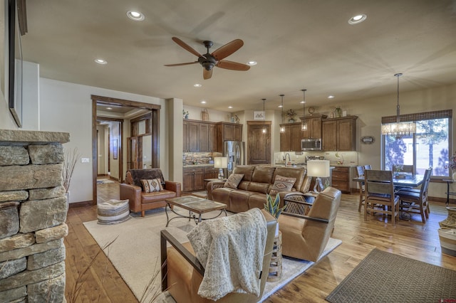 living area featuring recessed lighting, light wood-style flooring, and ceiling fan with notable chandelier