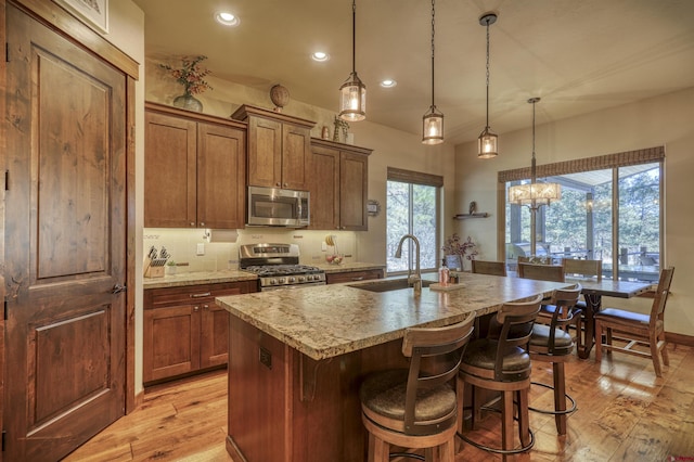 kitchen featuring a kitchen island with sink, a sink, appliances with stainless steel finishes, light wood finished floors, and a kitchen bar