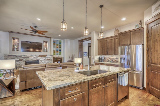 kitchen with light stone countertops, stainless steel appliances, light wood-style floors, a fireplace, and a sink