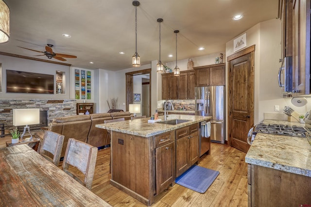 kitchen with stainless steel appliances, light stone counters, a sink, and light wood-style flooring