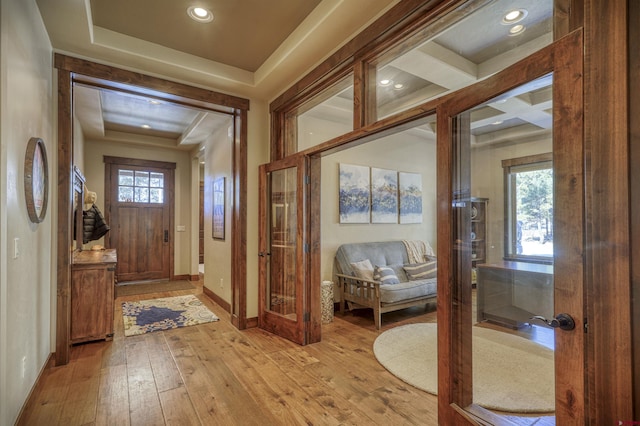 doorway with a tray ceiling, recessed lighting, light wood-style flooring, coffered ceiling, and baseboards