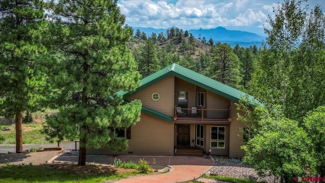 view of front facade with a balcony, crawl space, a mountain view, and a view of trees