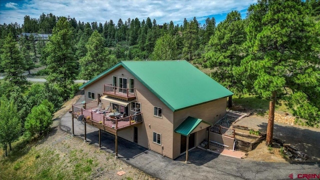 back of house with aphalt driveway, an attached garage, metal roof, a balcony, and a forest view