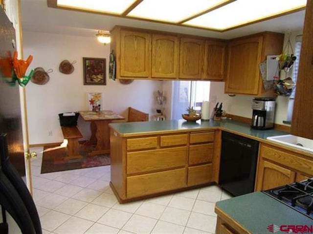kitchen with light tile patterned floors, a peninsula, a sink, black appliances, and brown cabinetry