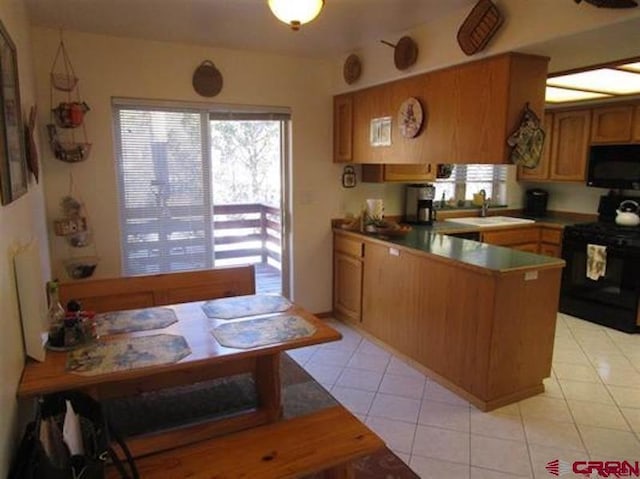 kitchen featuring brown cabinets, light tile patterned floors, a sink, a peninsula, and black appliances