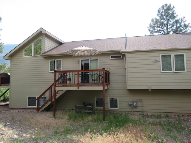 back of property with a deck, a shingled roof, and stairway