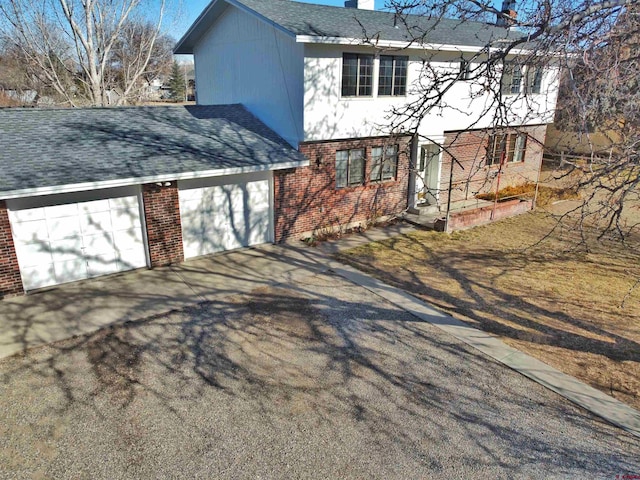 view of front of home featuring aphalt driveway, brick siding, a chimney, and roof with shingles