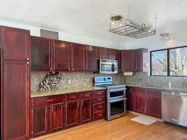 kitchen with stainless steel appliances, a sink, visible vents, light wood-style floors, and dark brown cabinets