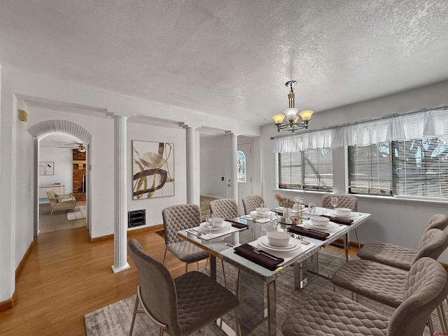 dining area featuring decorative columns, arched walkways, light wood-style flooring, a textured ceiling, and a notable chandelier