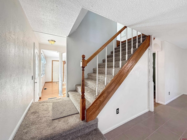 stairway featuring decorative columns, visible vents, baseboards, a textured wall, and a textured ceiling