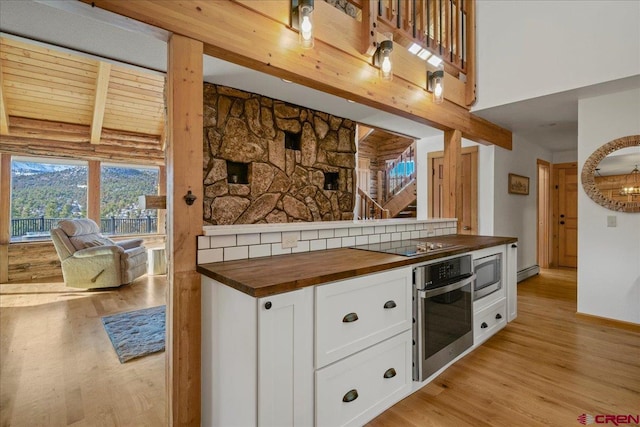 kitchen with stainless steel appliances, wood counters, white cabinetry, light wood finished floors, and beamed ceiling