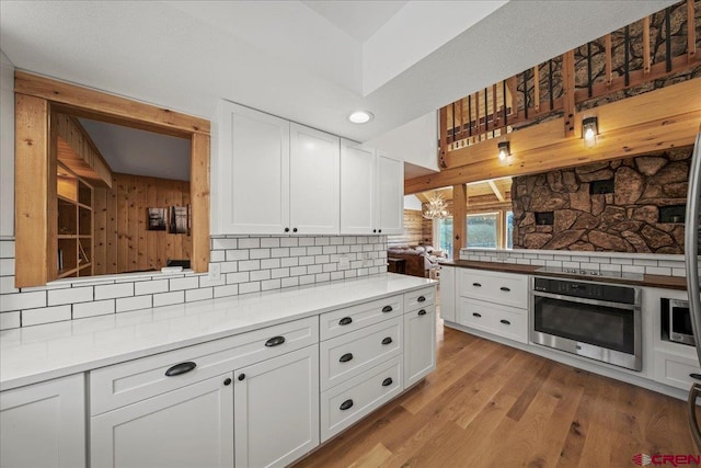 kitchen with stainless steel oven, white cabinets, light countertops, light wood-type flooring, and tasteful backsplash