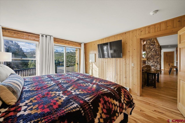 bedroom with light wood finished floors, wood walls, and access to exterior