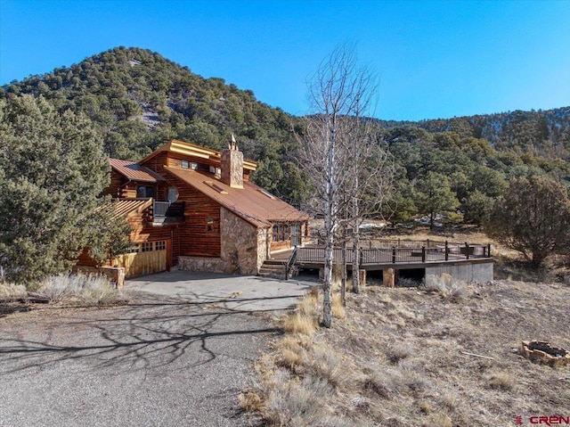 view of front of home with a deck with mountain view, metal roof, a view of trees, stone siding, and driveway