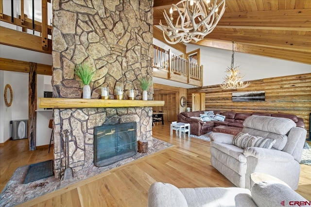 living area with high vaulted ceiling, a notable chandelier, a stone fireplace, and wood finished floors