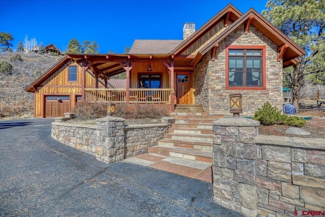 view of front of property with aphalt driveway, a chimney, board and batten siding, a garage, and stone siding