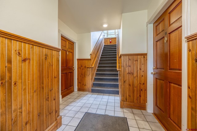 stairway featuring a wainscoted wall, tile patterned floors, and wood walls