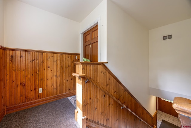 hallway featuring a wainscoted wall, carpet, wooden walls, and visible vents