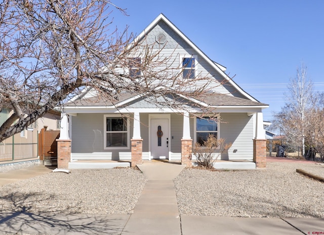 view of front of house featuring a shingled roof, covered porch, and fence