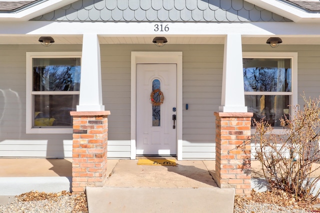 doorway to property with covered porch and a shingled roof