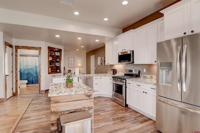 kitchen with light stone counters, stainless steel appliances, recessed lighting, light wood-style flooring, and white cabinets