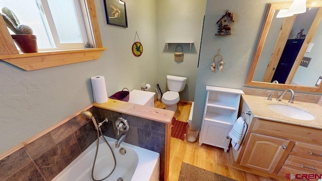 bathroom with a garden tub, vanity, toilet, and wood finished floors