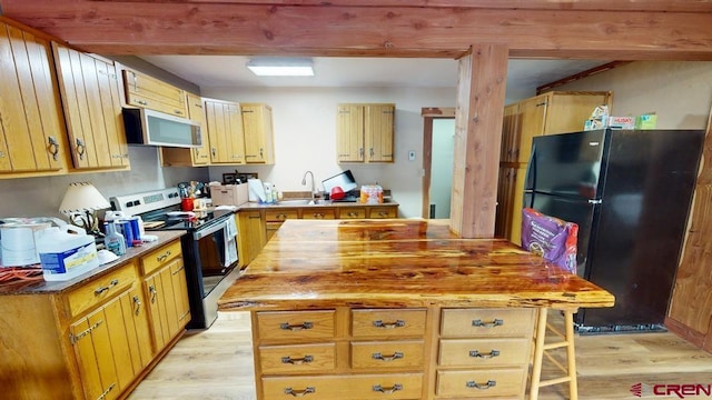 kitchen with appliances with stainless steel finishes, a sink, light wood-style flooring, and wood counters