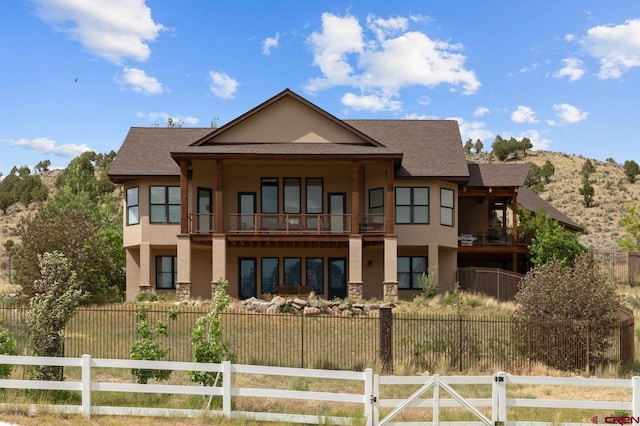 back of property with stucco siding, a fenced front yard, roof with shingles, and a balcony